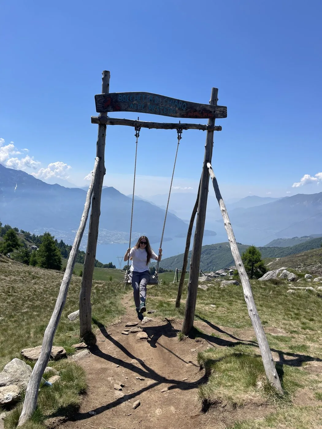 Iuliia on a wooden swing at a mountain viewpoint overlooking a lake and the Alps